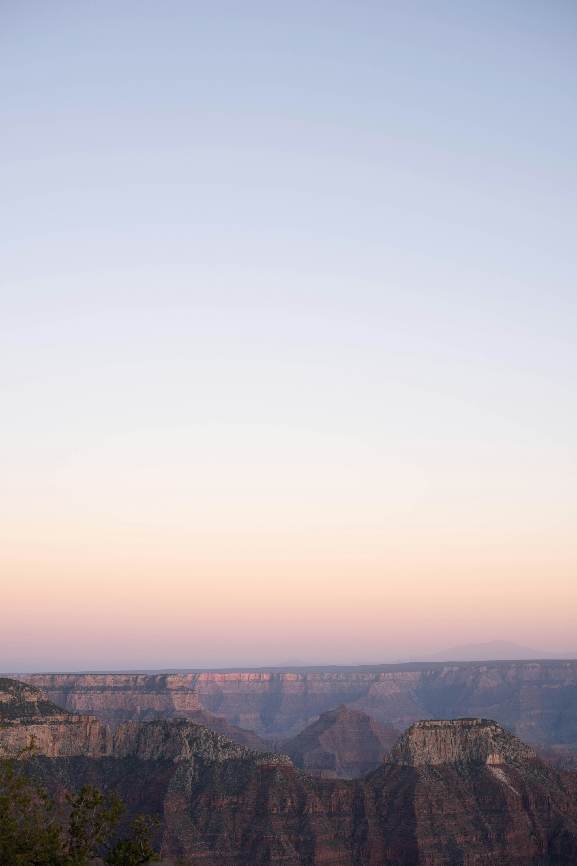 The Grand Canyon layered in violet, rust, and gold beneath a pale sunset sky