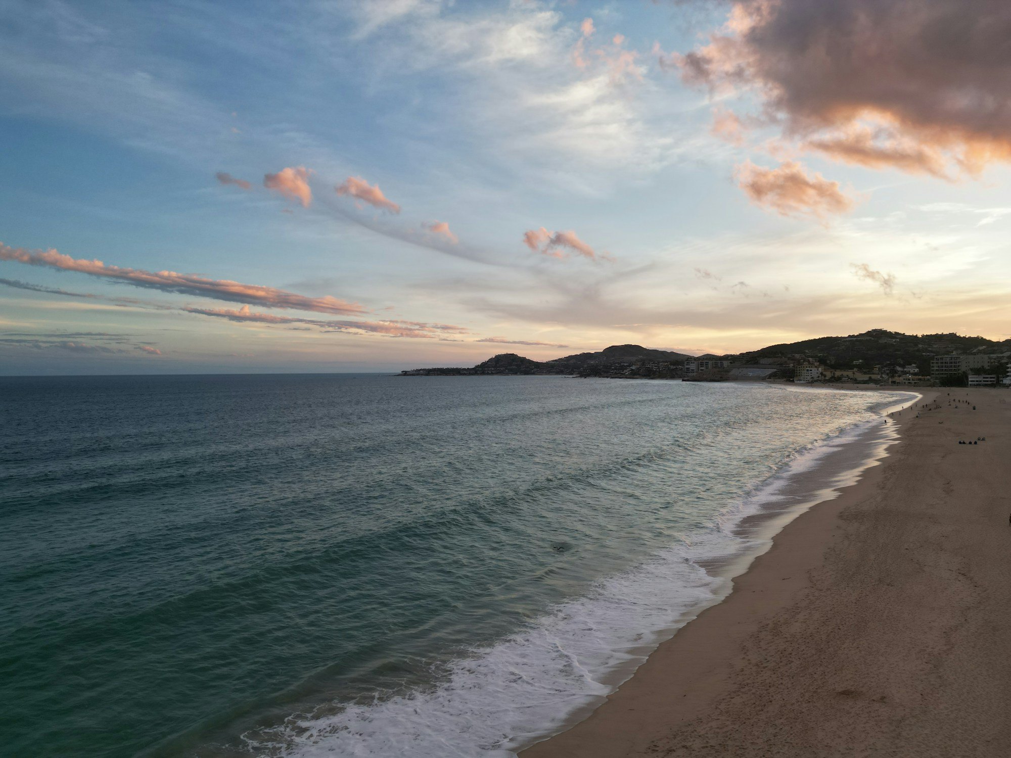Soft pink clouds above a curving beach and the ocean in Cabo San Lucas at sunset